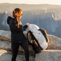 Woman in a hooded jacket adjusting her backpack on a rocky summit