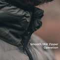 Close-up of a person wearing a dark gray puffer jacket, focusing on the zipper tab and pull tab, with the text 'Smooth YKK Zipper Operation' overlaid on the right side.