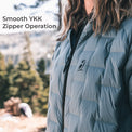 A close-up of a person wearing a light blue-gray puffer jacket outdoors, with the text 'Smooth YKK Zipper Operation' overlaid on the left side. The jacket has a black zipper and a small black YKK logo on the chest.