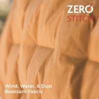 Close-up of a quilted fabric surface in a warm tan/camel color with the text 'ZERO STITCH' in the top right and 'Wind, Water, & Dust Resistant Fabric' in the bottom left.