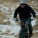 Cyclist mountain biking on a snowy trail while wearing a Ventus Active Hoodie