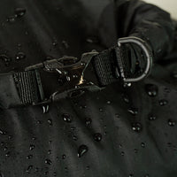 Extreme close-up of a water-resistant roll-top dry sack buckle closure with an attached D-ring, featuring water droplets on the durable coated fabric surface.