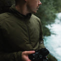Side profile of a photographer holding a camera outdoors while wearing a lightweight half-zip hooded jacket.