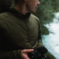 Side profile of a photographer holding a camera outdoors while wearing a lightweight half-zip hooded jacket.