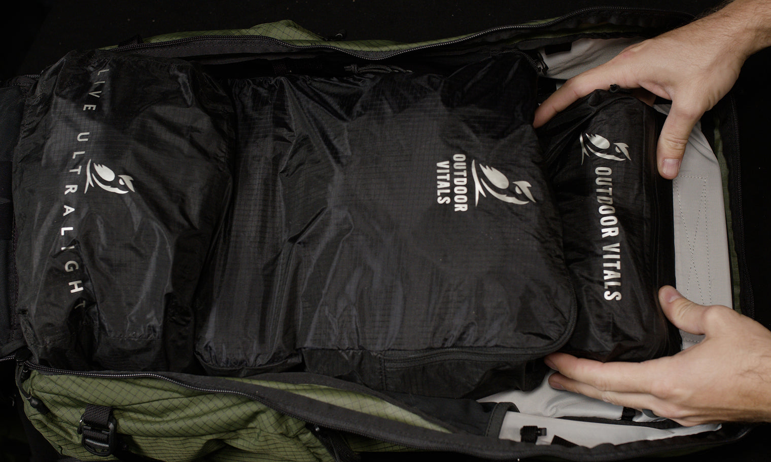 Overhead view of hands placing packing cubes and accessory pouches into the fully unzipped main compartment of the Outdoor Vitals KotaUL Ultralight Travel & Adventure Backpack.
