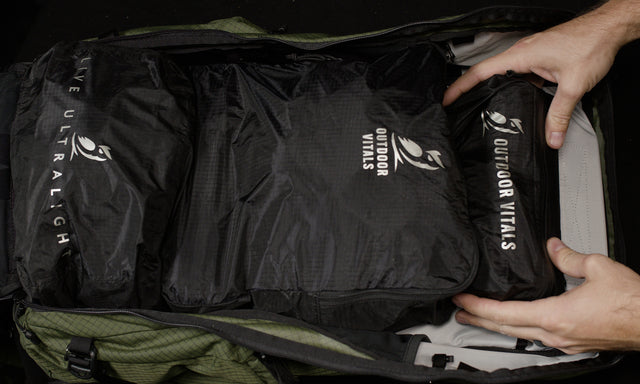 Overhead view of hands placing packing cubes and accessory pouches into the fully unzipped main compartment of the Outdoor Vitals KotaUL Ultralight Travel & Adventure Backpack.