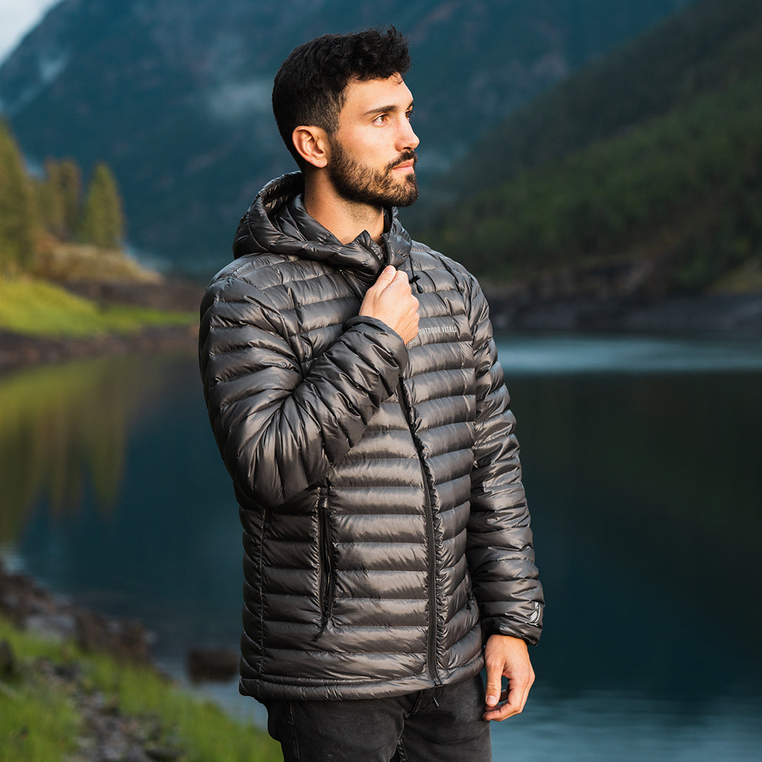 A man stands by a scenic mountain lake wearing a NovaUL jacket highlights the horizontal baffled quilting, a full-zip front, zippered hand pockets, and a fitted hood.