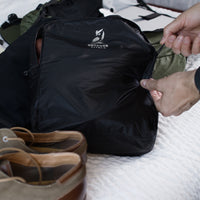 Close-up of hands pulling the zipper shut on a filled Outdoor Vitals packing cube while organizing travel gear alongside the KotaUL Ultralight Backpack.