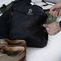 Close-up of hands pulling the zipper shut on a filled Outdoor Vitals packing cube while organizing travel gear alongside the KotaUL Ultralight Backpack.