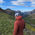 Rear view of a hiker wearing a hooded jacket looking out at mountain peaks.