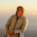 A man wearing a NovaPro down jacket and a beanie looking out at a sunset.
