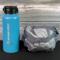 Packed ultralight rain jacket beside a water bottle for size comparison