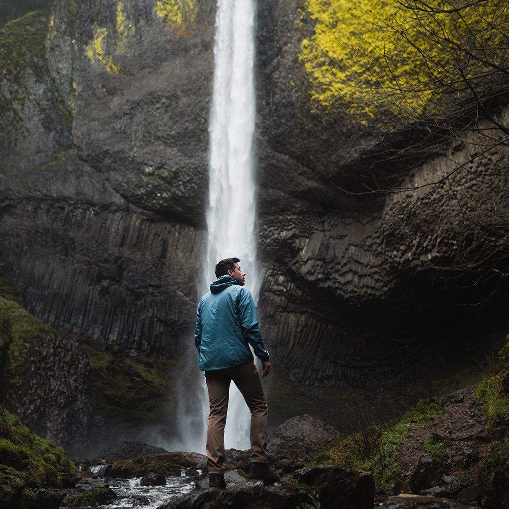 Rear view of a man looking up at a tall waterfall while wearing a Ventus Active Hoodie.